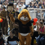 Alunos e mascotes PM Amigo Legal e Dare na cerimônia PROERD no Ginásio Poliesportivo, Extrema, 2025